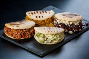 Comida latino-americana venezuelana, 4 arepas com recheios diferentes em uma mesa preta. Arepa com carne mechada, pepeada rainha, feijão preto com queijo branco e frango.